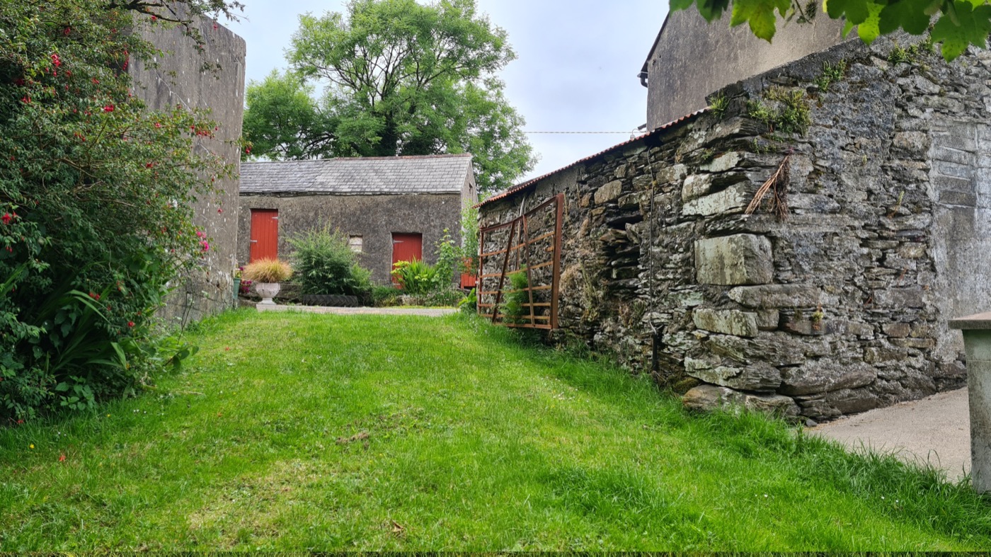 A grassy lane between stone walls leading to red-doored farm buildings at Gurrane