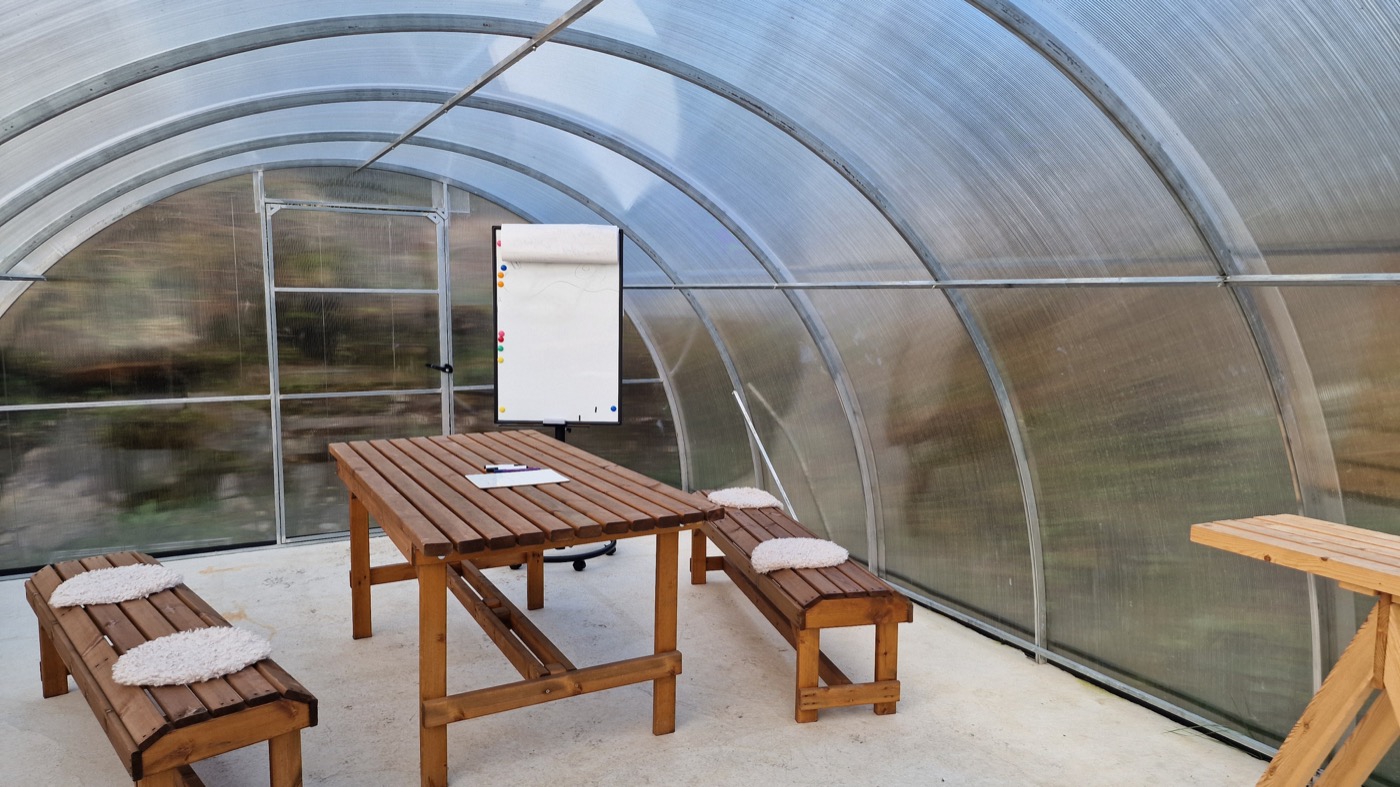 An empty polytunnel workshop set with a timber table, benches and a flip chart